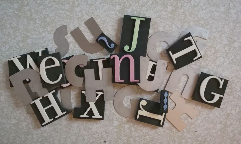 Durcheinanderliegende Buchstaben aus Aluminium und Moosgummi, die Buchstaben R-E-C-H-N-U-N-G liegen obenauf