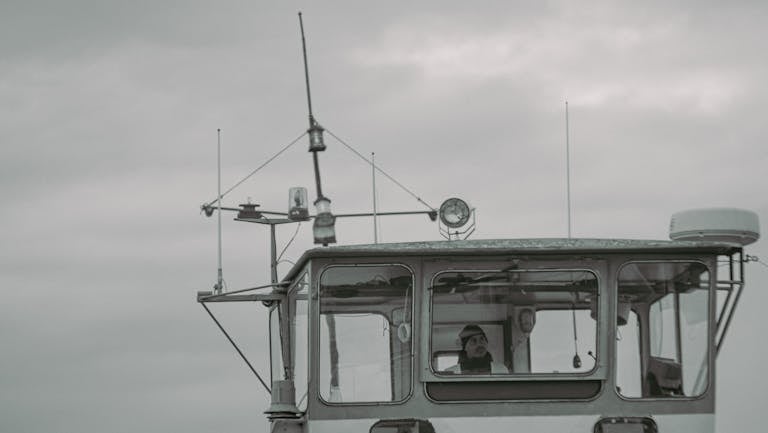 A captain stands on the bridge of a ship, navigating through cloudy weather.