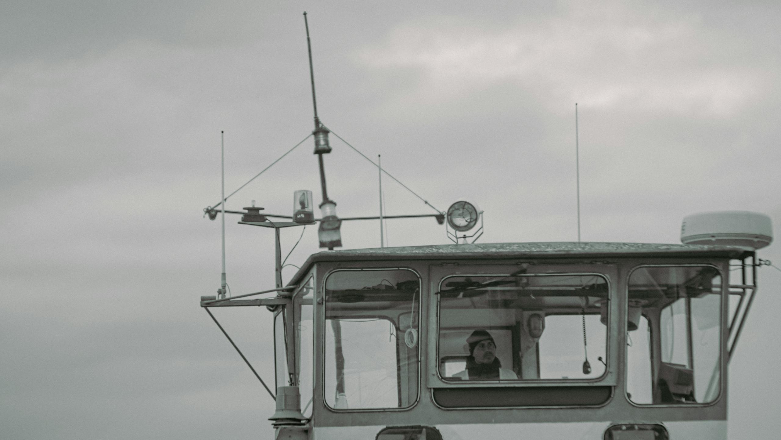 A captain stands on the bridge of a ship, navigating through cloudy weather.