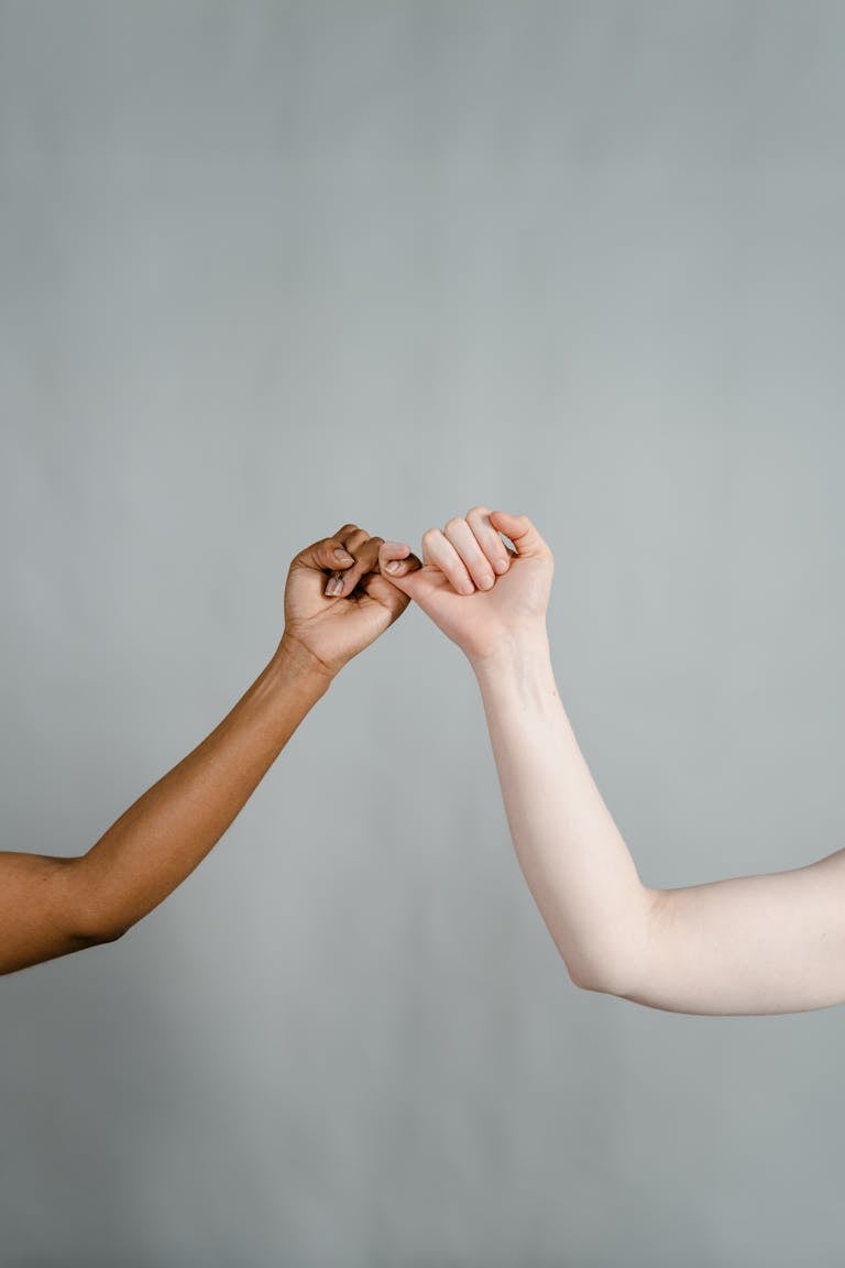Two diverse hands making a promise, symbolizing unity and friendship against a gray backdrop.